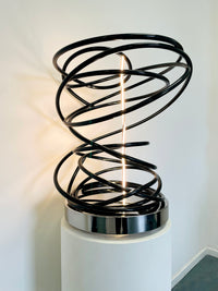 Illuminate your space with Mark Beattie's White in Tall Black Spiral, a unique sculpture featuring dimmable LED white light and painted copper on a mirror-polished stainless steel plinth. This one-of-a-kind masterpiece, measuring 67 x 54 x 52cm, is a captivating blend of light, texture, and contemporary design. Explore the artistic brilliance of White in Tall Black Spiral, available in different LED colors to suit your personal style and preferences.