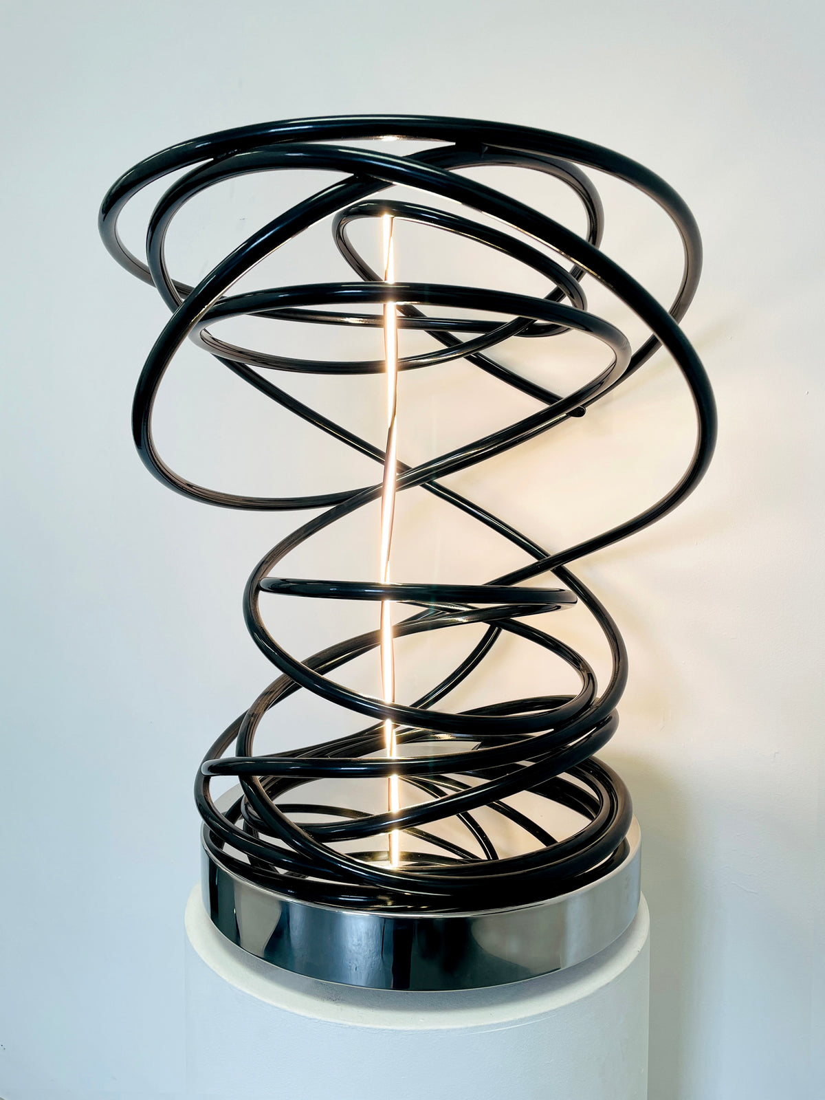 Illuminate your space with Mark Beattie's White in Tall Black Spiral, a unique sculpture featuring dimmable LED white light and painted copper on a mirror-polished stainless steel plinth. This one-of-a-kind masterpiece, measuring 67 x 54 x 52cm, is a captivating blend of light, texture, and contemporary design. Explore the artistic brilliance of White in Tall Black Spiral, available in different LED colors to suit your personal style and preferences.