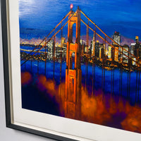 Framed art print of the Golden Gate Bridge at night, painted in vibrant blue, orange, and purple tones, shown in a black frame with a white mat. This is Bob Dylans depition of San Francisocs famous bridge 