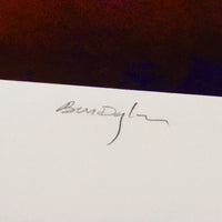 A close-up of a white card or paper with a small black handwritten signature, set against a dark reddish-brown background which is Bob Dylan's signature on one of his editioned prints