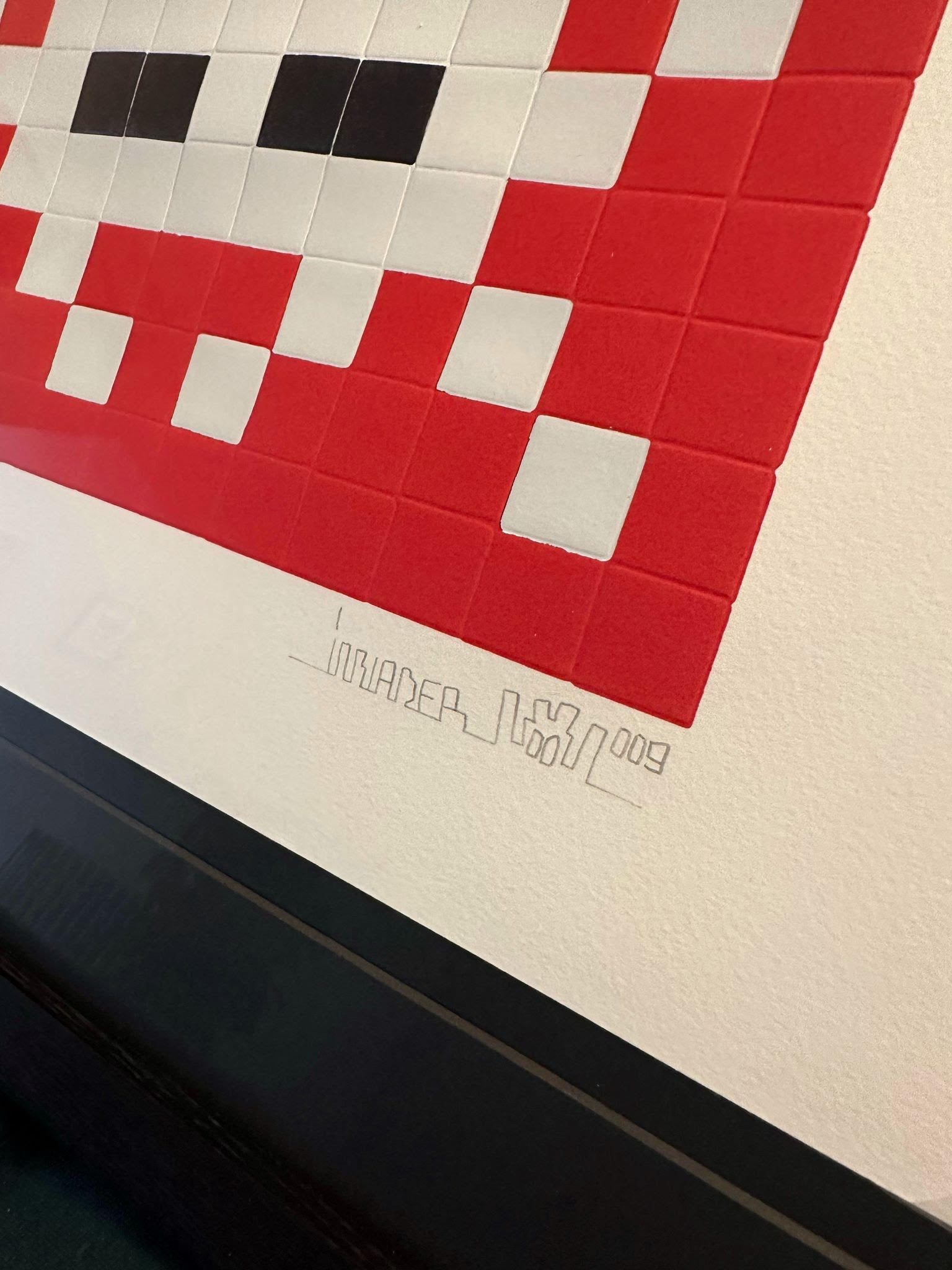 Invader Invasion red print in a black box frame with a close up of his signature