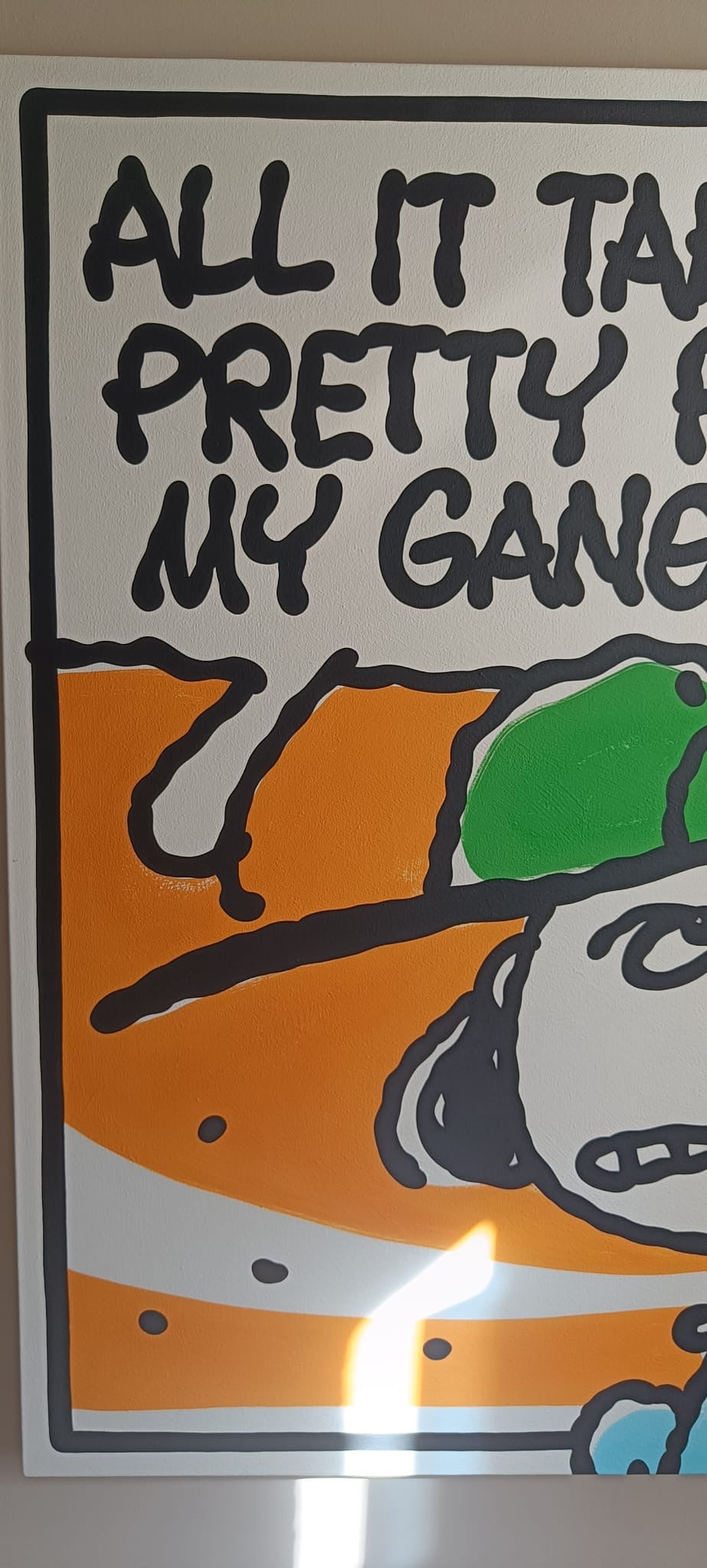 A square art print or poster featuring a cartoon-style illustration with the text 'ALL IT TAKES IS PRETTY HARD, MY GANG' in bold black lettering. The artwork features orange, green, white, and black shapes, with a bright glare near the bottom centre from the acrylic framing. 