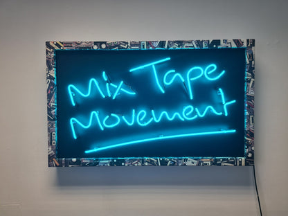Experience the nostalgia of Mix Tape Movement by Tony Spink. This one-of-a-kind artwork features turquoise neon on a wooden backing panel painted black, adorned with a collage-style frame depicting mix tapes. Measuring 60 x 98 cm, this original masterpiece is a unique fusion of neon art and musical nostalgia. Elevate your space with this distinctive neon artwork capturing the essence of the mix tape era in a warehouse 