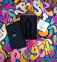 Rob Lenihans sculpture of a man from head to toe in black with his hood up in its presentation box on a graffiti background