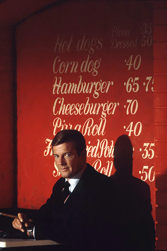 Terry O'Neill, Roger Moore as James Bond smoking a cigar in a diner on the film set of 'Live and let die', 1973 Limited edition fine art photograph by Terry O'Neill, featuring iconic portrait photography of celebrities and cultural figures. Available for sale at Smolensky Gallery