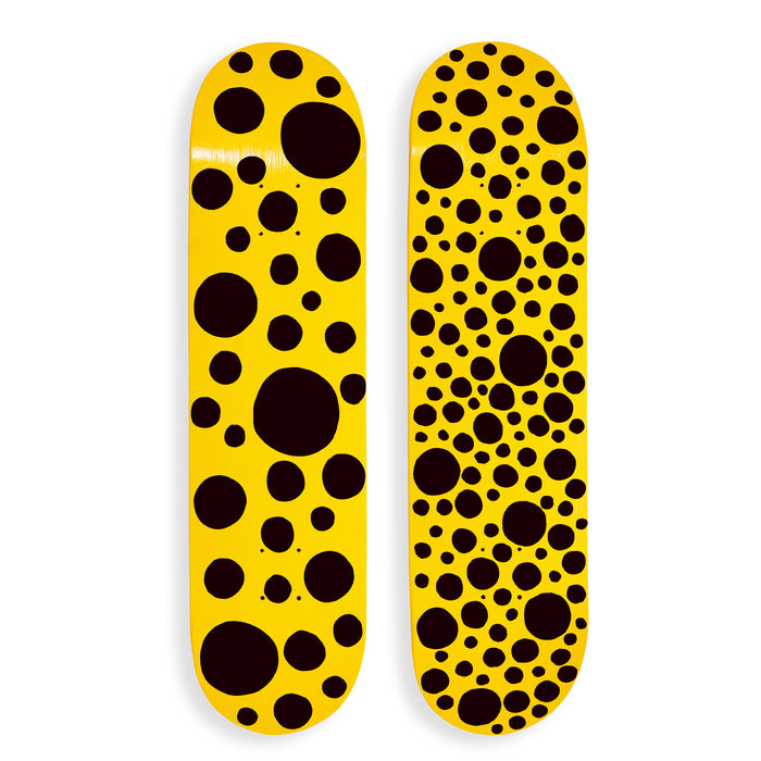 Two skateboard decks shown side by side on a white background, featuring a bold yellow and black spotted pattern reminiscent of cheese curds. One deck shows the top side with a few large black circles on a bright yellow background, while the other shows the underside with a dense pattern of black circles of varying sizes.