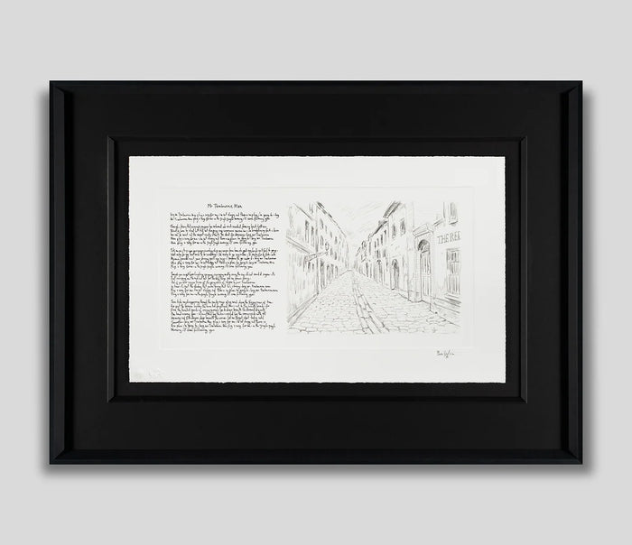 Framed black and white art print featuring a pencil-style sketch of a European street on the right and a block of text on the left, set in a black frame against a light gray background.