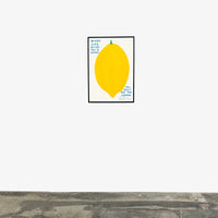An image of an artwork by David Shrigley titled 'When Life Gives You A Lemon' in a black frame hung on a white wall in a room with a grey floor. The piece features a large, cartoon-like depiction of a lemon, with text at the top right stating 'WHEN LIFE GIVES YOU A LEMON', and in the bottom right continuing 'YOU MUST EAT THE LEMON', 'ALL OF IT', 'INCLUDING THE SKIN'. This is a David Shrigley Poster or Print